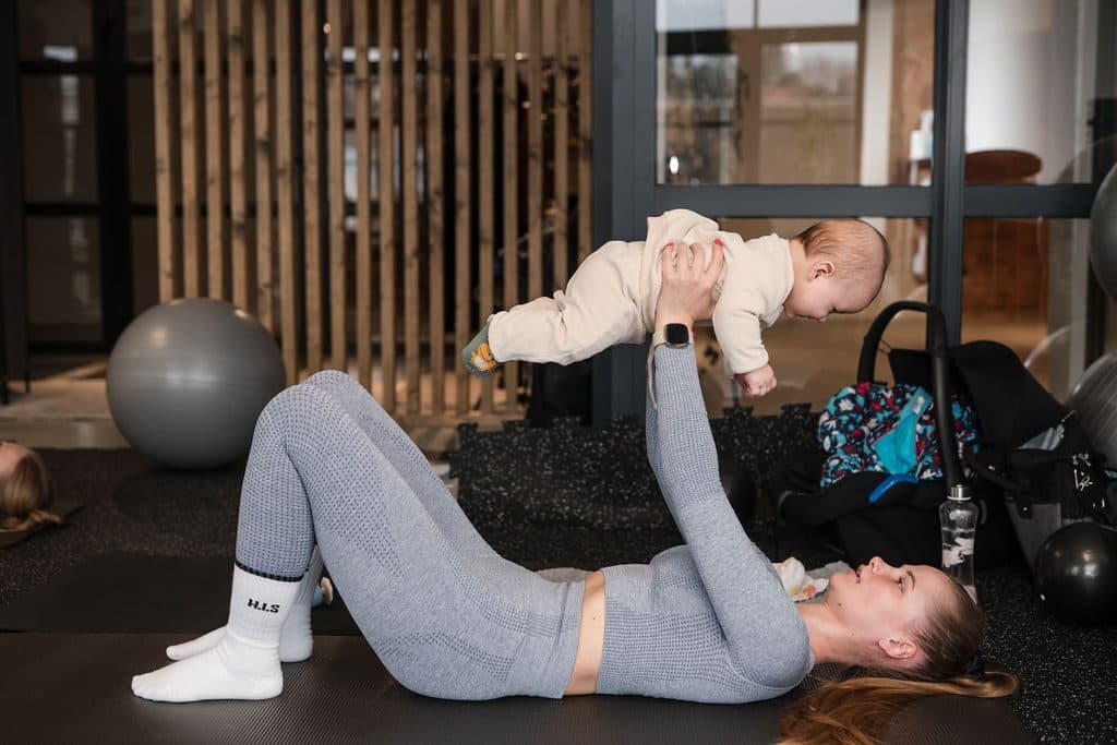 Mamos ir kūdikio mankšta: mama guli ant kilimėlio ir laiko kūdikį iškeltą virš savęs